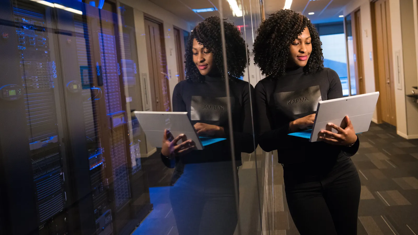 Two people holding laptops in a server room corridor